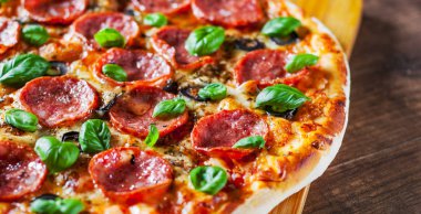 Pepperoni Pizza Mozzarella peyniri, salam, domates, zeytin, biber, baharat ve taze fesleğen. Ahşap masa arka plan üzerinde İtalyan pizza