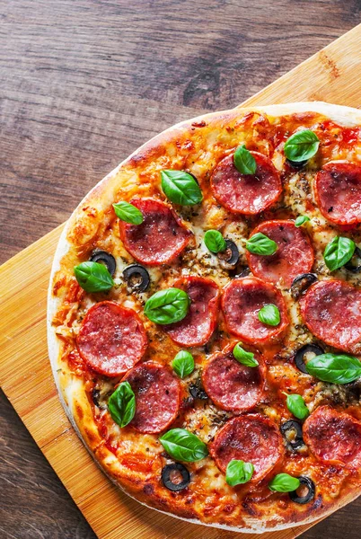 Pepperoni Pizza Mozzarella peyniri, salam, domates, zeytin, biber, baharat ve taze fesleğen. Ahşap masa arka plan üzerinde İtalyan pizza