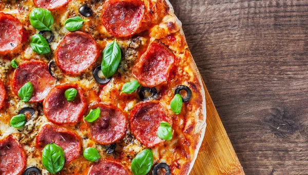 Pepperoni Pizza Mozzarella peyniri, salam, domates, zeytin, biber, baharat ve taze fesleğen. Ahşap masa arka plan üzerinde İtalyan pizza