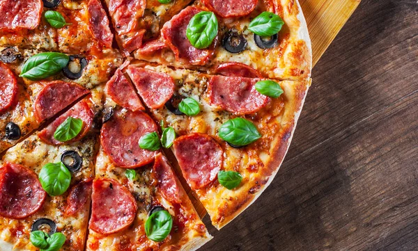 Pepperoni Pizza Mozzarella peyniri, salam, domates, zeytin, biber, baharat ve taze fesleğen. Ahşap masa arka plan üzerinde İtalyan pizza
