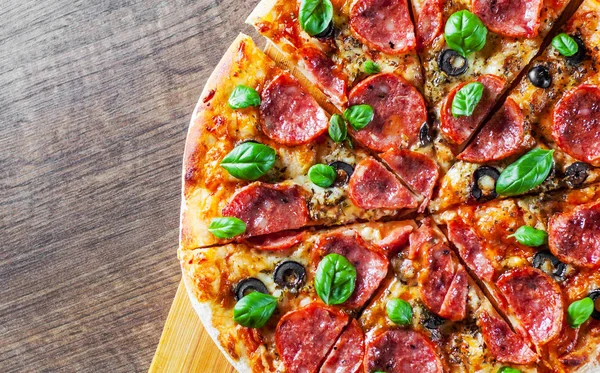 Pepperoni Pizza Mozzarella peyniri, salam, domates, zeytin, biber, baharat ve taze fesleğen. Ahşap masa arka plan üzerinde İtalyan pizza