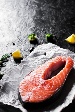 taze Çiğ somon biftek brokoli, limon, zeytin, biber ve koyu arka plan üzerinde aromatik otlar ile