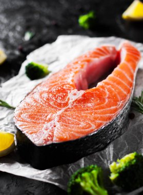 taze Çiğ somon biftek brokoli, limon, zeytin, biber ve koyu arka plan üzerinde aromatik otlar ile