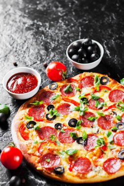 Pepperoni Pizza Mozzarella peyniri, salam, domates, zeytin, biber, baharat ve taze fesleğen. İtalyan pizza koyu arka plan üzerinde