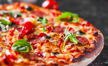 Mozzarella peyniri, salam, domates, zeytin, biber, baharat ve taze roka ile biberli Pizza. İtalyan pizza koyu arka plan üzerinde