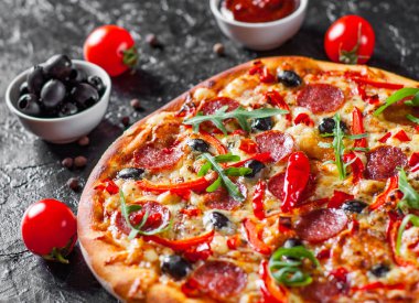Mozzarella peyniri, salam, domates, zeytin, biber, baharat ve taze roka ile biberli Pizza. İtalyan pizza koyu arka plan üzerinde