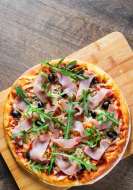 Mozzarella peyniri, jambon, biber, zeytin, et, domates sosu, baharat ve taze roka pizza. Ahşap arka plan üzerinde İtalyan pizza