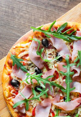 Mozzarella peyniri, jambon, biber, zeytin, et, domates sosu, baharat ve taze roka pizza. Ahşap arka plan üzerinde İtalyan pizza