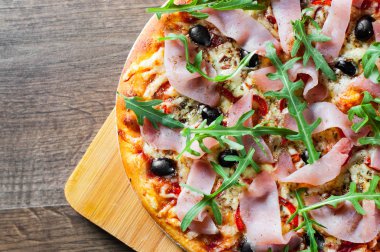 Mozzarella peyniri, jambon, biber, zeytin, et, domates sosu, baharat ve taze roka pizza. Ahşap arka plan üzerinde İtalyan pizza