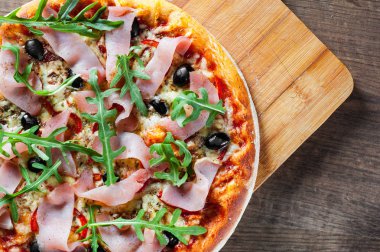 Mozzarella peyniri, jambon, biber, zeytin, et, domates sosu, baharat ve taze roka pizza. Ahşap arka plan üzerinde İtalyan pizza