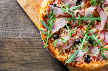 Mozzarella peyniri, jambon, biber, zeytin, et, domates sosu, baharat ve taze roka pizza. Ahşap arka plan üzerinde İtalyan pizza