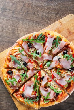 Mozzarella peyniri, jambon, biber, zeytin, et, domates sosu, baharat ve taze roka pizza. Ahşap arka plan üzerinde İtalyan pizza