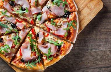 Mozzarella peyniri, jambon, biber, zeytin, et, domates sosu, baharat ve taze roka pizza. Ahşap arka plan üzerinde İtalyan pizza