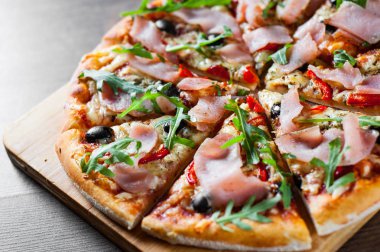 Mozzarella peyniri, jambon, biber, zeytin, et, domates sosu, baharat ve taze roka pizza. Ahşap arka plan üzerinde İtalyan pizza