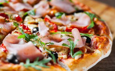 Mozzarella peyniri, jambon, biber, zeytin, et, domates sosu, baharat ve taze roka pizza. Ahşap arka plan üzerinde İtalyan pizza