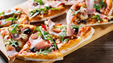 Mozzarella peyniri, jambon, biber, zeytin, et, domates sosu, baharat ve taze roka pizza. Ahşap arka plan üzerinde İtalyan pizza