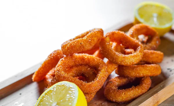fried squid rings breaded with lemon on wooden table background