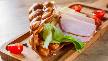 Jambon, peynir ve ahşap masa arka plan üzerinde sebze ile Hong Kong kabarcık waffle sandviç