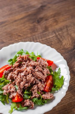 Ton balıklı salata roka ve domates ahşap masa arka plan üzerinde beyaz plaka ile
