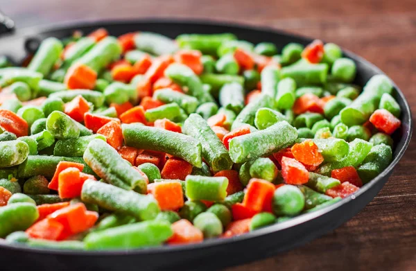 混合蔬菜 豌豆和胡萝卜在木制背景的铁锅里 — 图库照片