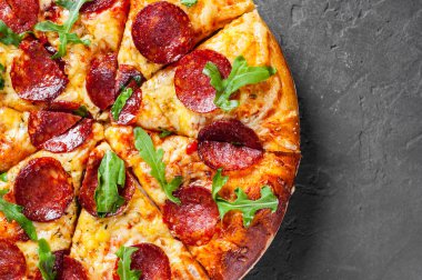 Mozzarella peyniri, salam, domates sos, biber, baharat ve taze roka ile biberli Pizza. İtalyan pizza koyu gri siyah arduvaz arka plan üzerinde