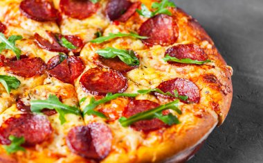 Mozzarella peyniri, salam, domates sos, biber, baharat ve taze roka ile biberli Pizza. İtalyan pizza koyu gri siyah arduvaz arka plan üzerinde