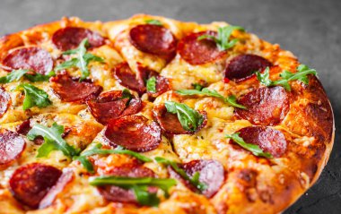 Mozzarella peyniri, salam, domates sos, biber, baharat ve taze roka ile biberli Pizza. İtalyan pizza koyu gri siyah arduvaz arka plan üzerinde