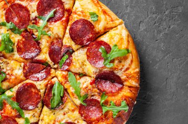 Mozzarella peyniri, salam, domates sos, biber, baharat ve taze roka ile biberli Pizza. İtalyan pizza koyu gri siyah arduvaz arka plan üzerinde