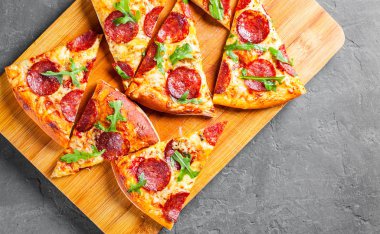 Mozzarella peyniri, salam, domates sos, biber, baharat ve taze roka ile biberli Pizza. İtalyan pizza koyu gri siyah arduvaz arka plan üzerinde