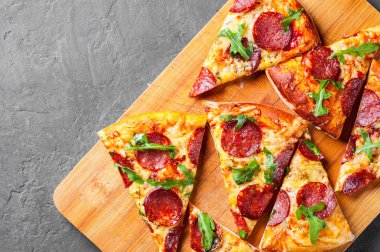 Mozzarella peyniri, salam, domates sos, biber, baharat ve taze roka ile biberli Pizza. İtalyan pizza koyu gri siyah arduvaz arka plan üzerinde