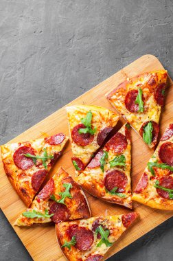 Mozzarella peyniri, salam, domates sos, biber, baharat ve taze roka ile biberli Pizza. İtalyan pizza koyu gri siyah arduvaz arka plan üzerinde