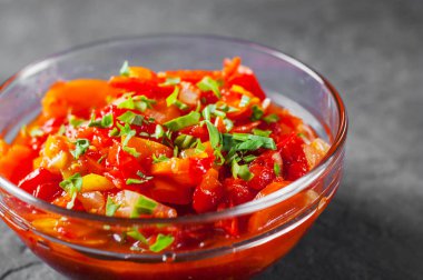 Domates, biber ve koyu gri siyah arduvaz arka plan üzerine cam kapta havuç ile Letcho