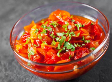 Domates, biber ve koyu gri siyah arduvaz arka plan üzerine cam kapta havuç ile Letcho