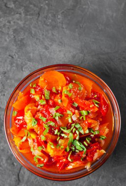 Domates, biber ve koyu gri siyah arduvaz arka plan üzerine cam kapta havuç ile Letcho