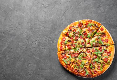 Pizza Mozzarella peyniri, mantar, jambon, domates sosu, sosis, biber, baharat ve taze roka. İtalyan pizza koyu gri siyah arduvaz arka plan üzerinde