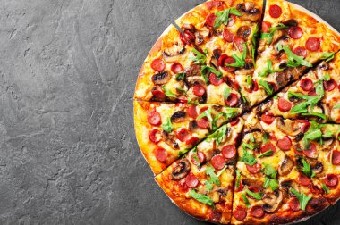 Pizza Mozzarella peyniri, mantar, jambon, domates sosu, sosis, biber, baharat ve taze roka. İtalyan pizza koyu gri siyah arduvaz arka plan üzerinde