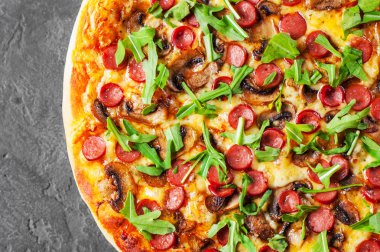 Pizza Mozzarella peyniri, mantar, jambon, domates sosu, sosis, biber, baharat ve taze roka. İtalyan pizza koyu gri siyah arduvaz arka plan üzerinde