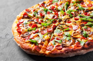 Pizza Mozzarella peyniri, mantar, jambon, domates sosu, sosis, biber, baharat ve taze roka. İtalyan pizza koyu gri siyah arduvaz arka plan üzerinde