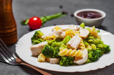 Düdük makarna tavuk göğsü ve koyu gri siyah arduvaz arka plan üzerine beyaz tabak Brokoli Salatası ile