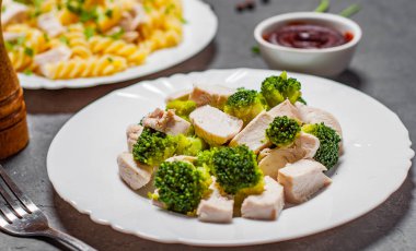 Düdük makarna tavuk göğsü ve brokoli ile koyu gri siyah arduvaz arka plan üzerine beyaz tabakta tavuk göğsü ile