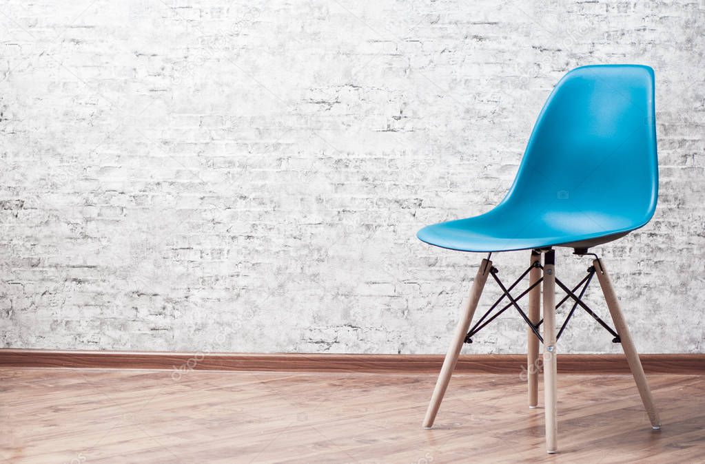 Modern blue plastic chair in an empty room with wooden floor on gray Brick Wall Background with copy space.
