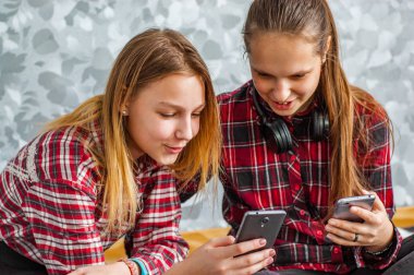 Gri duvar arka planda evde bir kanepede otururken cep telefonları kullanarak iki genç Genç kız