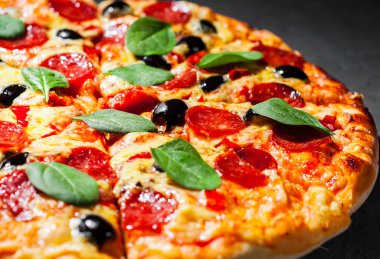 Mozzarella peyniri, salam, zeytin, biber, Baharat ve Taze ıspanak ile Pepperoni Pizza. Koyu gri siyah arduvaz arka plan üzerinde İtalyan pizza