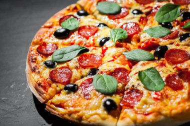 Mozzarella peyniri, salam, zeytin, biber, Baharat ve Taze ıspanak ile Pepperoni Pizza. Koyu gri siyah arduvaz arka plan üzerinde İtalyan pizza