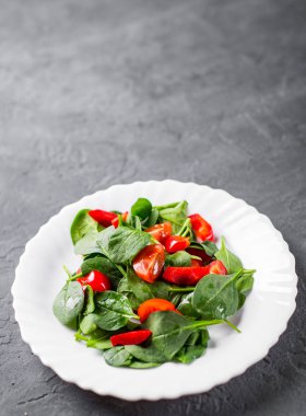 Biberli ıspanak salatası ve koyu gri arka planda beyaz tabakta domates.