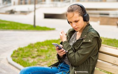 Uzun saçlı genç genç esmer kız Açık portre. bankta oturan cep telefonu kullanarak müzik dinleyen genç kadın
