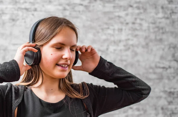 灰色の壁の背景にワイヤレスヘッドフォンで音楽を聴く長い髪を持つ若いティーンエイジャーブルネットの女の子の肖像画 — ストック写真