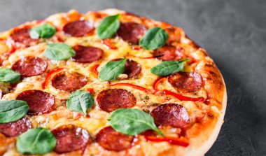 Mozzarella peynirli Pepperoni Pizza, salam, biber, baharat ve taze ıspanak. Koyu gri arka planda İtalyan pizzası