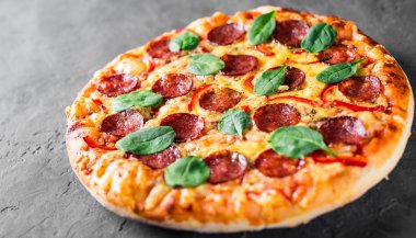Mozzarella peynirli Pepperoni Pizza, salam, biber, baharat ve taze ıspanak. Koyu gri arka planda İtalyan pizzası