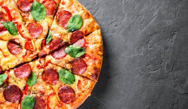 Mozzarella peynirli Pepperoni Pizza, salam, biber, baharat ve taze ıspanak. Koyu gri arka planda İtalyan pizzası